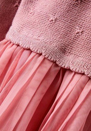Pink dress with a knitted top featuring small raised dots, transitioning to a pleated tulle skirt. Edged with a scalloped, sparkly band.