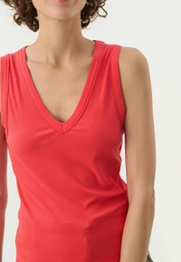 Rød ribbet tanktop med dyb V-hals og brede skulderstropper. Blød tekstur og tætsiddende silhuet, ideel til lag-på-lag.