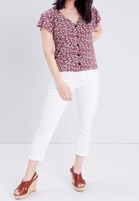 Chemisier à motif floral rouge avec des manches courtes à volants. Associé à un pantalon blanc ajusté et des sandales compensées marron.