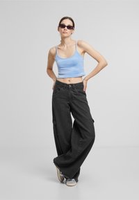 Top corto de tirantes azul claro, pantalones cargo negros de pierna ancha con dobladillo deshilachado, gafas de sol negras y zapatillas deportivas grises. Tejido suave con bolsillos.