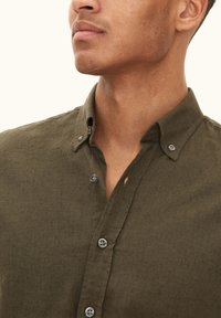 Olijfgroen button-up shirt van structuurstof, met een klassieke kraag, vier knopen en een open knop bij de hals.