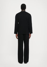 Crna majica dugih rukava i široke hlače od teksturiranog materijala, s opuštenim krojem i jednostavnim, čistim dizajnom.