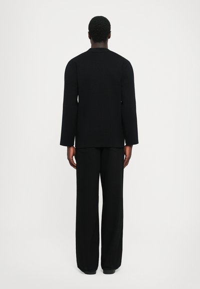 Must tume, pikkade varrukatega pluus ja laiad püksid, valmistatud tekstuurilisest kangast, millel on mugav lõige ja lihtne, selge disain.