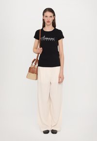 Zwarte katoenen t-shirt met witte "Armani Exchange" logo, beige geplooide wijde broek, bruine schoudertas, zwarte platte schoenen.