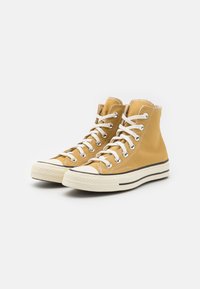 High-top sneakers made of yellow canvas, featuring white laces, a rubber sole, black stripe, and contrasting toe cap.
