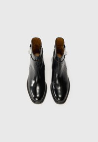 Bottines en cuir noir avec une finition lisse, un bout pointu, une fermeture éclair sur le côté et un détail de coutures contrastantes le long de la semelle.