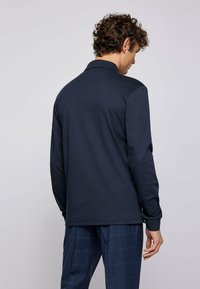 Navy long-sleeve polo shirt with a collared neckline, soft texture, and minimalistic design. Features long sleeves and a straight hem.