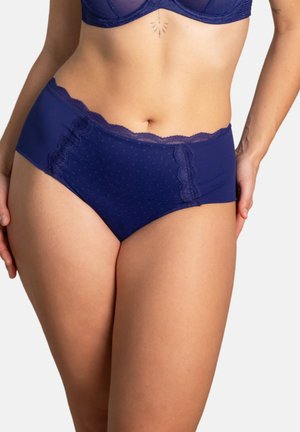 Frau trägt dunkelblaue, hochtaillierte Slip mit Spitzenbesatz und dezentem Pünktchenmuster, vom mittleren Oberkörper bis zu den oberen Oberschenkeln gezeigt.