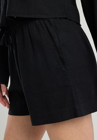 Mustat pellavashortsit, joissa on joustava vyötärö ja sivutaskut, rento malli ja sileä pinta.