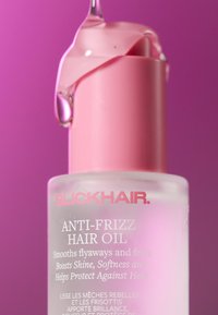 Bottiglia di vetro rosa satinato contenente olio anti-crespo per capelli con tappo rosa. Olio trasparente goccia dalla parte superiore. Testo bianco che mostra il nome del prodotto e i benefici.