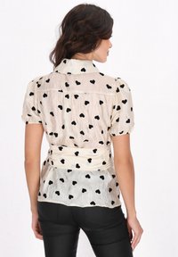 Durchsichtige beige Bluse mit schwarzem Herzmuster, Puffärmeln und tailliertem Schnitt. Geschmeidige Textur mit Kragen und gerafftem Rücken.