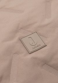 Zacht roze stof met een textuurpatroon en een vierkante, geperste logopatch met het label "Jollein" in een neutrale tint.