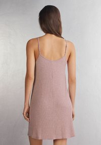 Jasnoróżowa sukienka z prążkowanego materiału z cienkimi regulowanymi ramiączkami, z okrągłym dekoltem z tyłu oraz rozszerzanym dołem. Miękka tkanina o subtelnej teksturze.