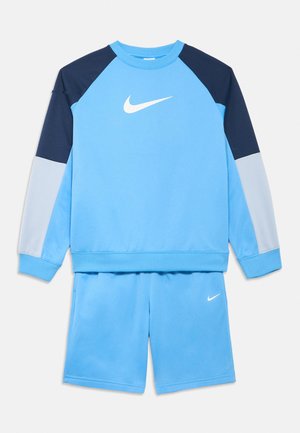 Svetlomodrá mikina Nike s tmavomodrými a svetlosivými rukávmi, v kombinácii so svetlomodrými šortkami, oboje s bielymi logami Nike swoosh.