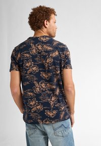 Camisa de manga corta azul marino con un patrón floral marrón claro, que presenta una textura suave y un ajuste holgado, combinada con unos jeans de denim.