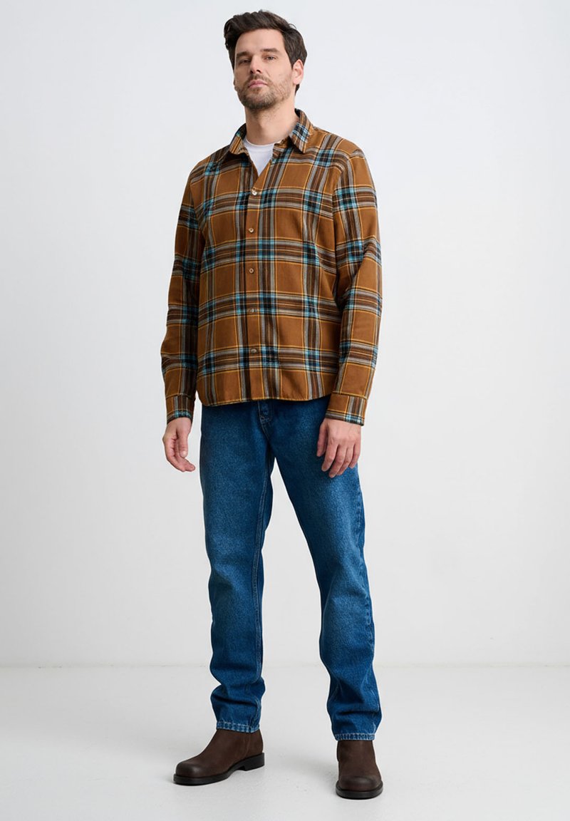 Brązowa koszula w kratę zapinana na guziki z błękitnymi akcentami, zestawiona z niebieskimi dżinsami i brązowymi butami. Koszula ma kołnierzyk i długie rękawy.