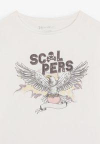 Camiseta blanca con un diseño impreso de un águila con las alas extendidas, un corazón y la palabra "SCALPERS" arriba, contorneada en negro.