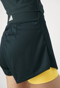 Svarta fuktavvisande shorts med en tight passform, featuring en bred midja och gula underställsynliga nedanför. Heat.Rdy-märket ingår.
