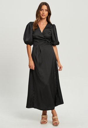 Black satin wrap dress with puff sleeves, a deep V-neckline, a side slit, and a smooth texture, complementing tan high-heeled sandals.
