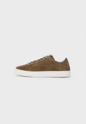 Bruine suede sneaker met een ronde neus, witte rubberen zool en vetersluiting. Kenmerkt zich door subtiele stiksels en een laag profiel ontwerp.
