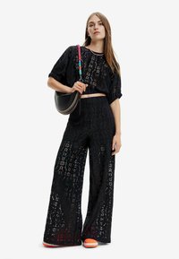 Sorte blonde to-delte sæt bestående af en cropped top med pufærmer og brede bukser. Sættet er kombineret med en sort taske og farverige sko.