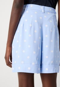 Light blue shorts made from smooth fabric, featuring white polka dots, pleated front, and a flat waistband with belt loops.
