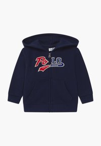 Felpa blu navy con zip realizzata in tessuto morbido, con tasche frontali e logo ricamato "Polo Ralph Lauren" in rosso e blu sul petto.