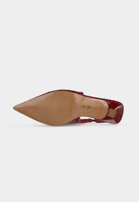 Chaussure rouge à talons hauts avec bout pointu vue de la semelle, avec une semelle lisse couleur fauve et un embout de talon texturé.