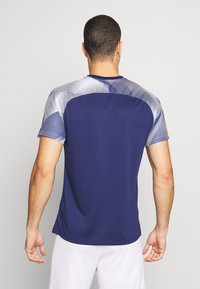 Námořnické tričko s krátkým rukávem určené pro sport, s texturovaným zadním dílem a kontrastním stříbrným grafickým vzorem na ramenou. Hladká tkanina, kulatý výstřih.