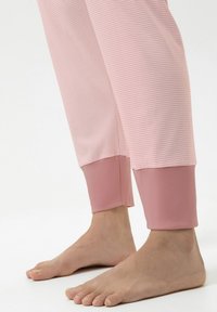 Pantalon de pyjama à rayures rose clair avec un revers uni rose. Le tissu semble doux, avec une coupe décontractée et une longueur raccourcie, laissant les pieds nus.