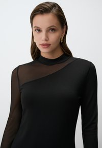 Zwarte lange mouwen jurk met een doorzichtige zwarte schouderpaneel, hoge halslijn, slim fit ontwerp en gladde, textuurstof.