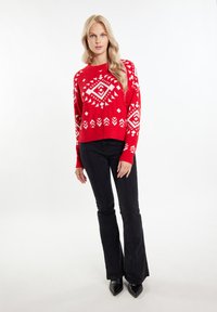 Pulover tricotat roșu cu modele geometrice albe, mâneci lungi și croială scurtă, asociat cu pantaloni negri evazați și tocuri negre ascuțite.