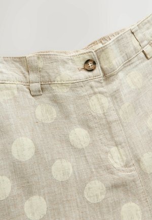 Beežid linased püksid suurte valgete täppidega, vööaasadega, ees nööpidega kinnitatavad ja nähtava esipoeega neutraalsel taustal.