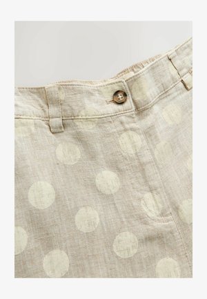 Beige linnedbukser med store hvide polkaprikker, bæltestropper, forreste knaplukning og en synlig forlomme på neutral baggrund.