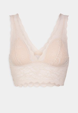Bralette en dentelle de couleur nude clair, avec des bords festonnés et des bonnets triangulaires, ornée d'un motif floral et d'une texture lisse et extensible.