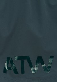 Mørkt stof med blanke sorte bogstaver, der danner det delvise ord "ATW" trykt nær sømkanten.