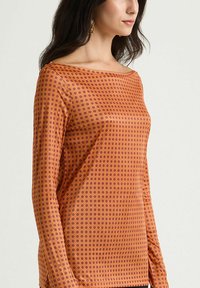 Top arancione a maniche lunghe con motivo a puntini viola, scollo a barca e tessuto leggero e morbido.