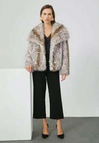 Faux fur jacket with a wide collar in light grey and brown tones. Paired with black wide-leg trousers and black heels. Large gold earrings.