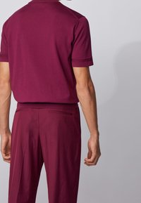 Polo a maglia bordeaux con maniche corte, colletto a coste e pantaloni bordeaux abbinati. Tessuto liscio con tasche laterali discrete.