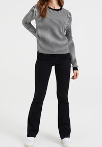 Pull en maille à carreaux noirs et blancs avec manches longues, poignets et ourlet côtelés. Associé à un jean noir évasé et des baskets blanches.