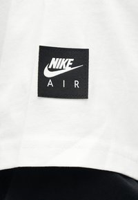 Μαύρο τετράγωνο με το λογότυπο Nike Air ραμμένο πάνω σε λευκό ύφασμα, με μαύρο φόντο υφάσματος.