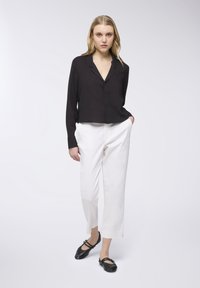 Blusa nera con bottoni e maniche lunghe, abbinata a pantaloni bianchi su misura e scarpe nere basse. Tessuto liscio, design minimalista.