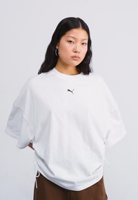 Hvit oversized T-skjorte laget av bomull, med korte ermer og rund hals. Lite svart Puma-logo på brystet. Justerbare sidetrekkinger.