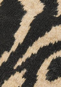 Primo piano di tessuto lavorato a maglia nero e beige con strisce frastagliate e irregolari che ricordano un motivo a stampa animale.