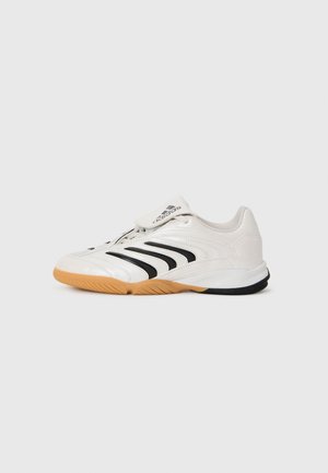 White athletic shoe with black stripes, rubber gum sole, textured upper, and Velcro strap on the tongue. Smooth materials with rounded shape.