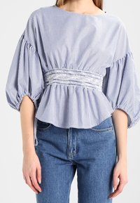 Blå och vit randig blus med vid halsringning, ballongärmar, samlad midja och mjukt tyg. Kombinerad med ljusblåjeans.