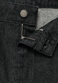 Zwarte spijkerbroek van denim met een zilveren rits en een metalen knoop met de gravure "JEANS 1984"; gestructureerde stof met lichte verticale strepen.