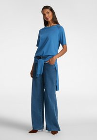 Blå kortärmad topp i kombination med vida denimbyxor. Toppen har en rund halsringning; byxorna har en knytdekal och är gjorda av mjuk denim.