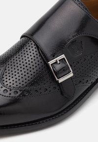 Black leather shoe with perforated design, a silver buckle accent, and smooth finish. Features a rounded toe and sturdy sole.
