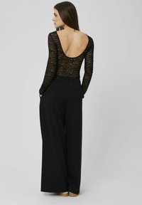 Body en dentelle noire à manches longues et décolleté plongeant au dos, associé à un pantalon noir taille haute à jambes larges. Tissu lisse et coupe ajustée.